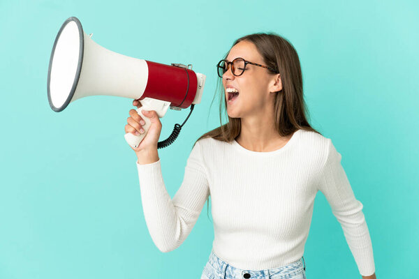 Молодая женщина на изолированном синем фоне кричит через мегафон, чтобы объявить что-то в боковом положении