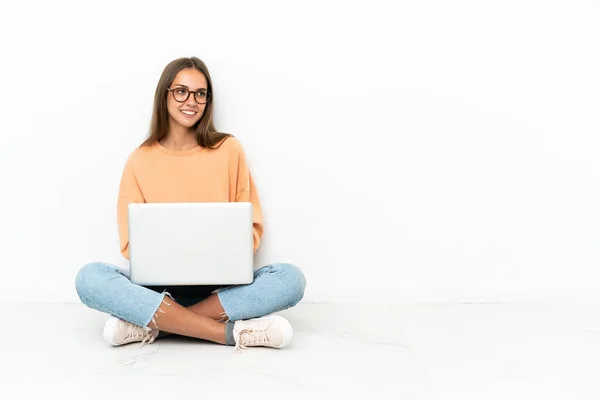 一个拿着笔记本电脑坐在地板上 双臂交叉 快乐的年轻女人 — 图库照片