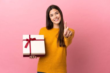 Genç Brezilyalı kız pembe arka planda bir hediye tutuyor ve parmağını kaldırıyor.