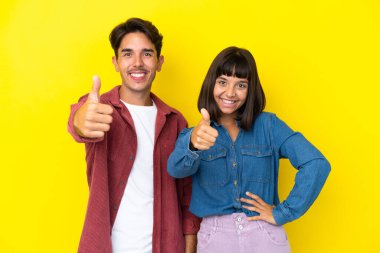 Genç melez çift sarı arka planda izole edilmiş. İyi bir şey olduğu için iyi bir jest yapıyorlar.