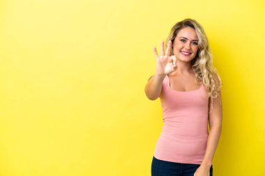 Sarı arka planda izole edilmiş genç Brezilyalı kadın mutlu ve parmaklarıyla üçe kadar sayıyor