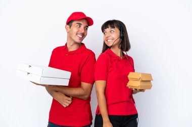 Beyaz arka planda izole edilmiş pizza ve burgerleri olan genç teslimatçı çift gülümseyerek omzunun üzerinden bakıyor.