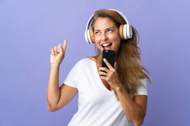 Mor arka planda izole edilmiş orta yaşlı Brezilyalı bir kadın cep telefonuyla müzik dinliyor ve şarkı söylüyor.