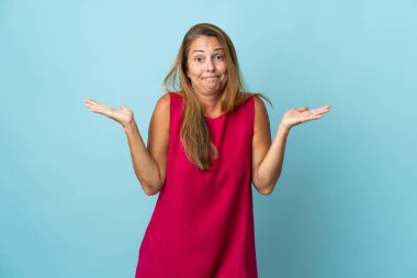 Orta yaşlı Brezilyalı bir kadın mavi arka planda izole edilmiş. Şüpheleri var ve ellerini kaldırıyor.