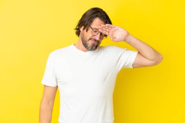 Yaşlı Hollandalı adam sarı arka planda izole edilmiş, yorgun ve hasta bir ifadeyle.