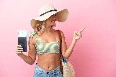 Yaz tatilinde mayo giymiş genç Brezilyalı bir kadın pembe arka planda izole edilmiş bir şekilde bir ürün sunmak için kenarı işaret ediyor.