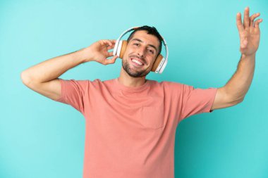 Genç yakışıklı beyaz adam mavi arka planda izole edilmiş müzik ve dans dinliyor.