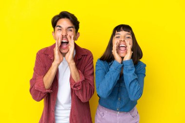 Genç melez çift sarı arka planda izole edilmiş bağırıyor ve bir şey duyuruyorlar.
