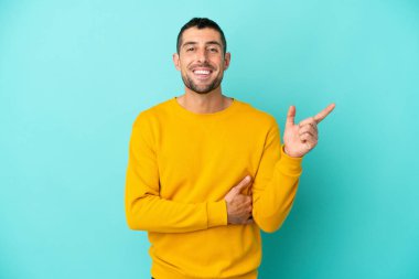 Mavi arka planda izole edilmiş yakışıklı beyaz adam mutlu ve dik duruyor.