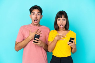 Mavi arka planda cep telefonu tutan genç melez çift sağa bakarken şaşırmış ve şok olmuştu.