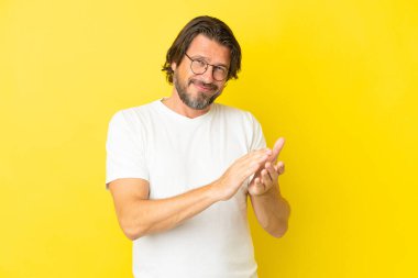 Yaşlı Hollandalı adam sarı arka planda izole edilmiş alkışlıyor.