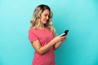Mavi arka planda izole edilmiş genç Brezilyalı kadın cep telefonuyla mesaj ya da e-posta gönderiyor