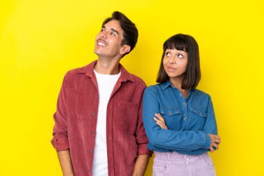 Sarı arka planda soyutlanmış genç melez çift kollarını kalçalarına dayayıp gülüyor.