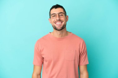 Mavi arka planda izole edilmiş yakışıklı beyaz adam mutlu bir ifadeyle gözlüklü.