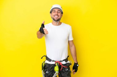 Genç kaya tırmanışçısı, sarı arka planda izole edilmiş, iyi bir anlaşma için el sıkışıyor.