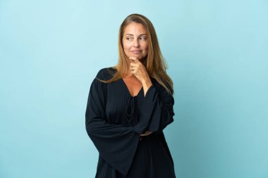 Mavi arka planda izole edilmiş orta yaşlı Brezilyalı kadın yan tarafa bakıyor.