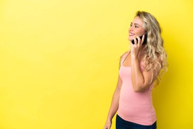 Sarı arka planda izole edilmiş genç Brezilyalı kadın cep telefonuyla sohbet ediyor.