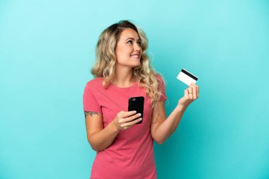 Genç Brezilyalı bir kadın mavi arka planda izole edilmiş ve kredi kartıyla alışveriş yapıyor.