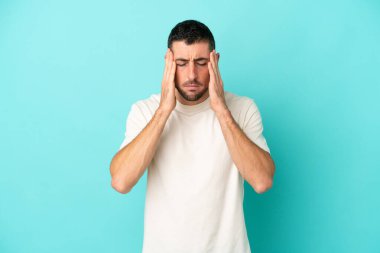 Mavi arka planda yalnız ve başı ağrıyan yakışıklı beyaz bir adam.