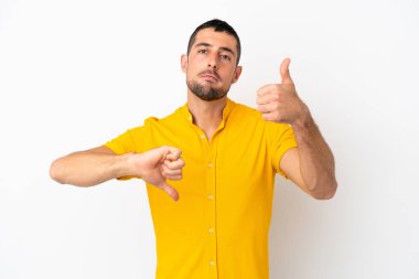 Beyaz arka planda izole edilmiş yakışıklı beyaz adam iyiye-kötüye işaret yapıyor. Evet ya da hayır arasında kararsız