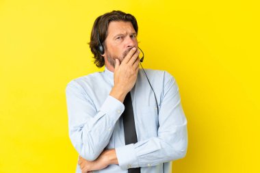 Tele pazarlamacı Hollandalı adam sarı arka planda izole edilmiş bir kulaklıkla çalışıyor sağa bakarken şaşırmış ve şok olmuş.