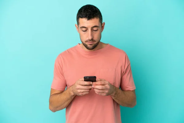 Junge Schöne Kaukasische Mann Isoliert Auf Blauem Hintergrund Mit Mobiltelefon — Stockfoto