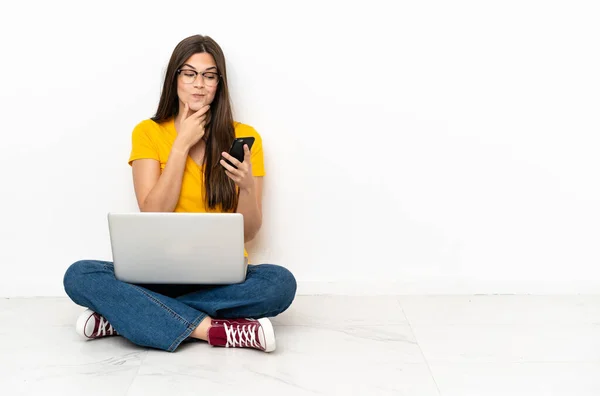 一个拿着笔记本电脑的年轻女人坐在地板上思考着 传达着一个信息 — 图库照片