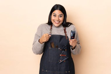 Genç Kolombiyalı kadın kuaför bej arka planda izole edilmiş bir şekilde zaferi kutluyor.