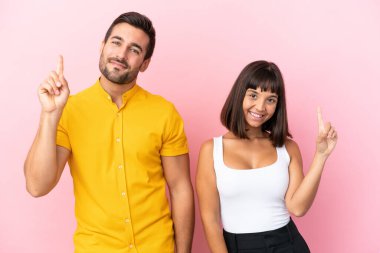 Pembe arka planda izole edilmiş genç bir çift en iyinin işareti olarak parmağını kaldırıyor.