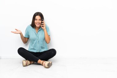 Genç kız yerde oturuyor ve cep telefonuyla birileriyle sohbet ediyor.