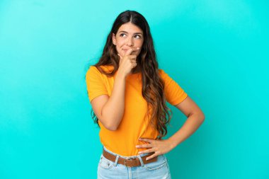 Kafkasyalı genç bir kadın mavi arka planda izole edilmiş. Şüpheleri var ve kafası karışmış bir yüz ifadesi var.