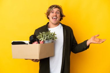 Sarışın adam, sarı arka planda izole edilmiş, şok olmuş yüz ifadesiyle bir kutu dolusu şey alırken hamle yapıyor.