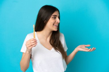 Mavi arka planda diş fırçalayan beyaz bir kadın. Şaşırtıcı bir yüz ifadesi var.