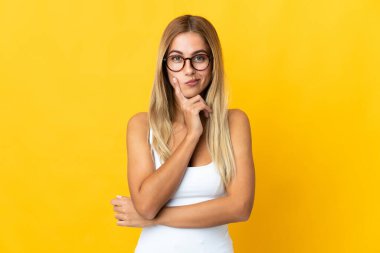 Sarışın genç kadın sarı arka planda izole edilmiş ve düşünüyor