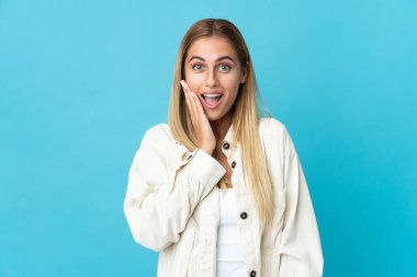 Genç sarışın kadın mavi arka planda izole edilmiş, şaşırmış ve şok olmuş bir yüz ifadesi var.
