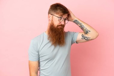 Pembe arka planda izole edilmiş genç, beyaz bir adam. Kafasını kaşırken şüpheleri var.