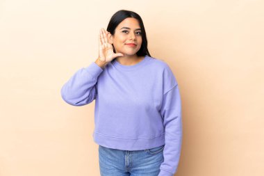 İzole edilmiş arka planda yaşayan genç Latin bir kadın. Kulağına elini sürerek bir şeyler dinliyor.