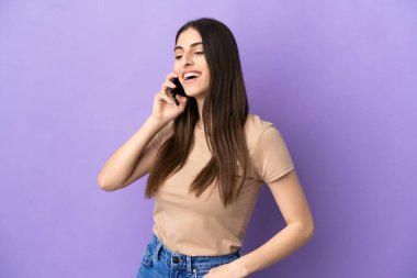 Mor arka planda izole edilmiş cep telefonu kullanan beyaz bir kadın yana bakıyor ve gülümsüyor.