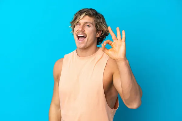 Yakışıklı Sarışın Adam Mavi Arka Planda Izole Edilmiş Parmaklarıyla Işaret — Stok fotoğraf