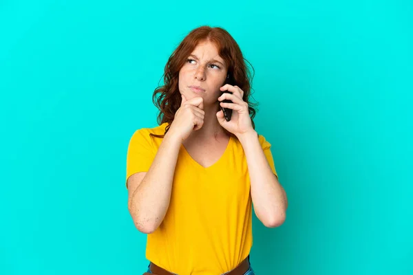 Teenager Načervenalé Žena Pomocí Mobilního Telefonu Izolované Modrém Pozadí Pochybnostmi — Stock fotografie