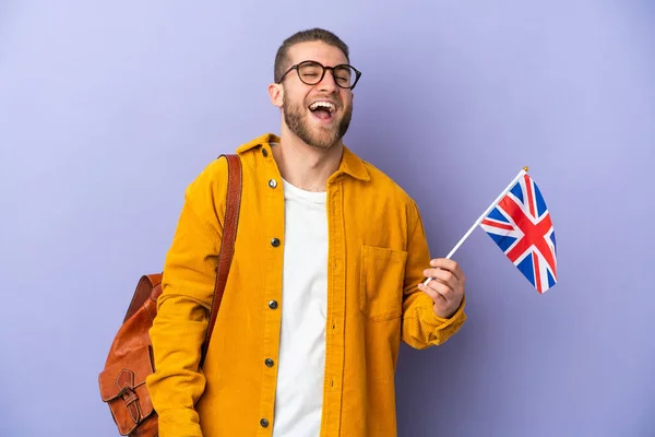 年轻的高加索男子举着一面英国国旗 被紫色背景的笑声隔开 — 图库照片