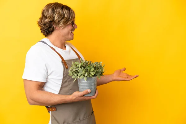 Gardener Ξανθιά Άνθρωπος Κρατώντας Ένα Φυτό Απομονωμένο Κίτρινο Φόντο Έκφραση — Φωτογραφία Αρχείου