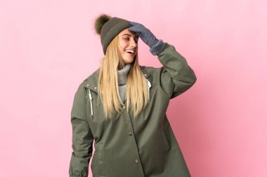 Pembe arka planda izole edilmiş, kış şapkalı genç bir kadın. Çok gülümsüyor.