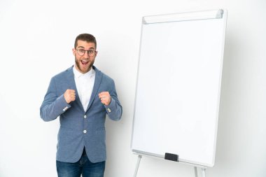 Beyaz arka planda izole edilmiş beyaz panoda sunum yapan genç iş kadını galibiyetini kutluyor.