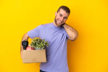Genç Kafkasyalı, sarı arka planda izole edilmiş şeylerle dolu bir kutuyu kaldırırken hamle yapıyor.