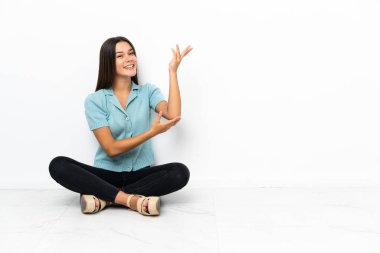 Genç bir kız yerde oturuyor. Davet edildiği için ellerini yana açıyor.