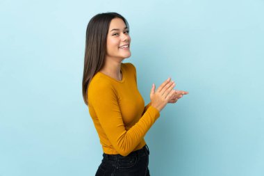 Mavi arka planda izole edilmiş genç kız alkışlıyor.