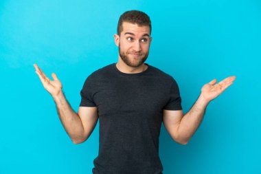 Mavi arka planda izole edilmiş yakışıklı beyaz adam şüpheli hareketler yapıyor.