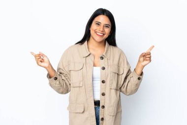 Beyaz arka planda izole edilmiş genç Latin kadın parmak uçlarını işaret ediyor ve mutlu.