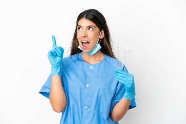 Dişçi kadın beyaz arka planda aletleri tutarken bir fikir öne sürüp işaret ediyor.